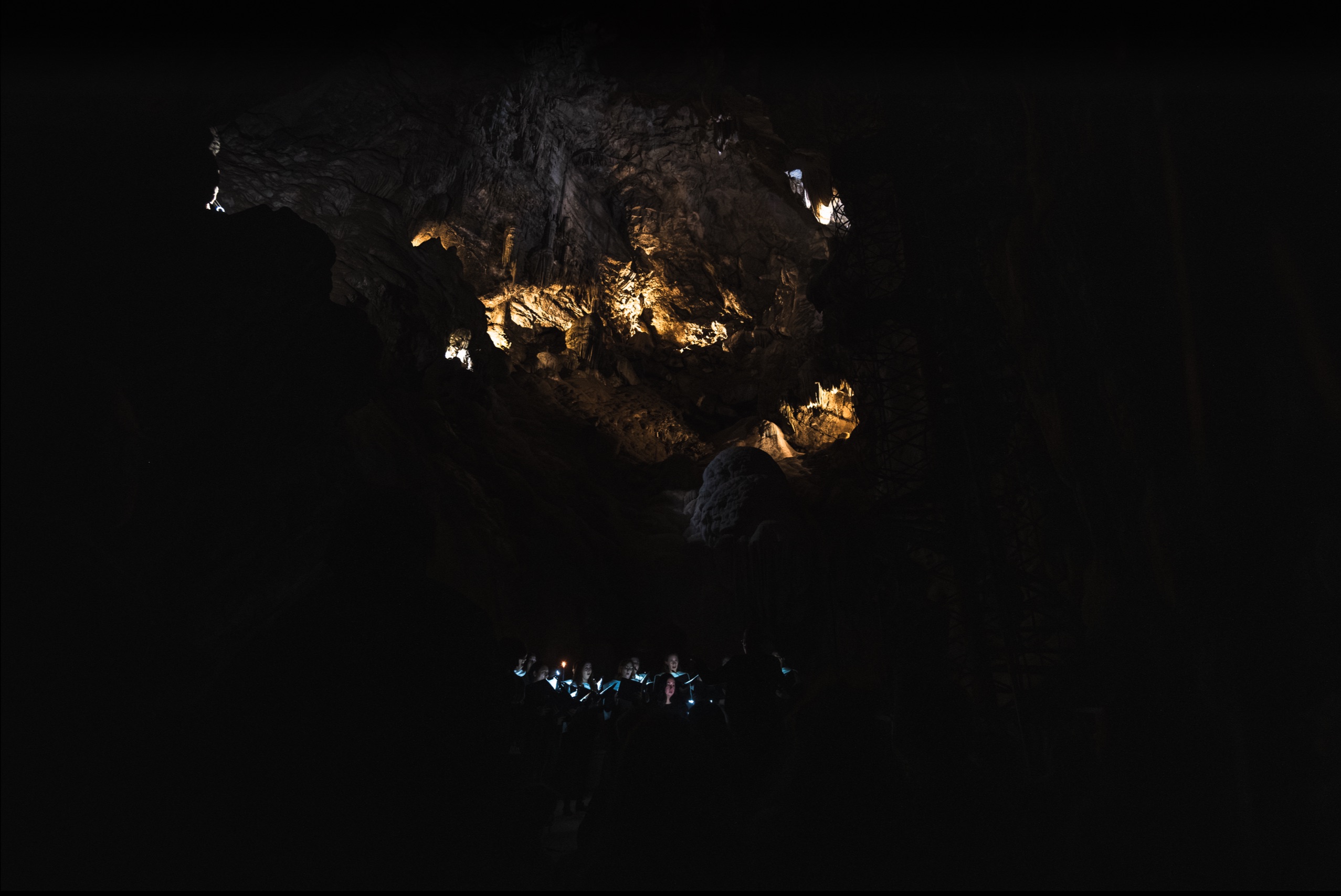 A choir performing by candlelight at the base of a vast cavern